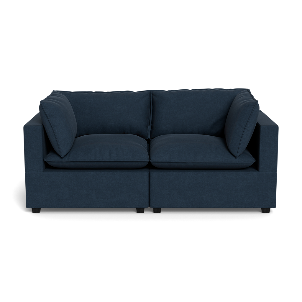 The Kova Pillow Cushion Sofa 86" is a modern, dark blue upholstered sofa with wide armrests and four large cushions, displayed front-facing against a plain black background.